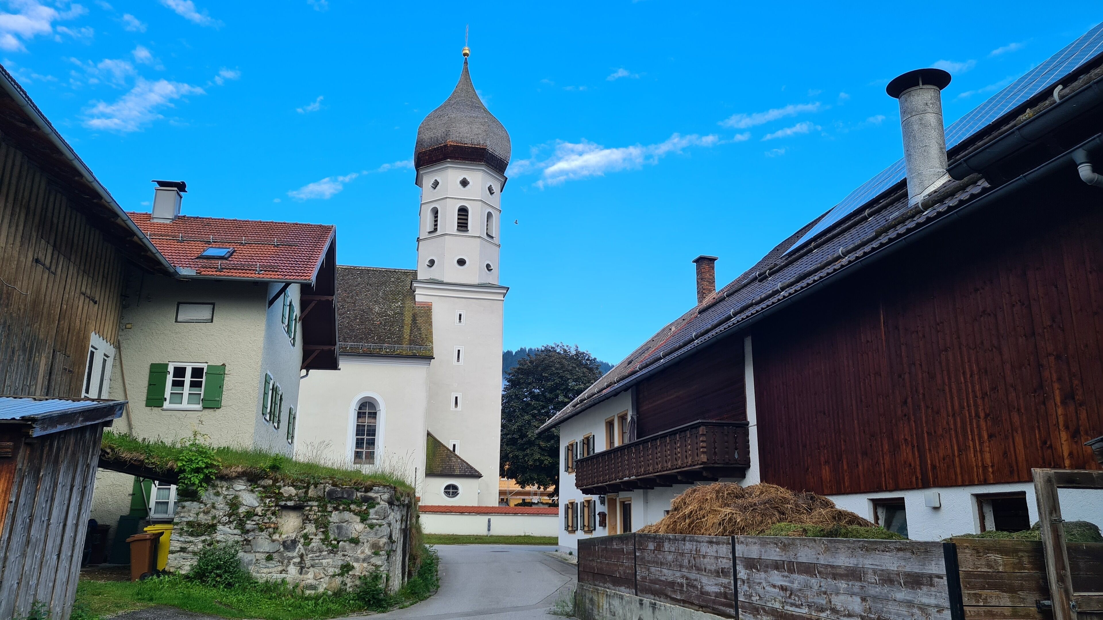Una calle estrecha que lleva a una iglesia con una torre alta, rodeada de edificios tradicionales con fachadas de madera y tejados inclinados.