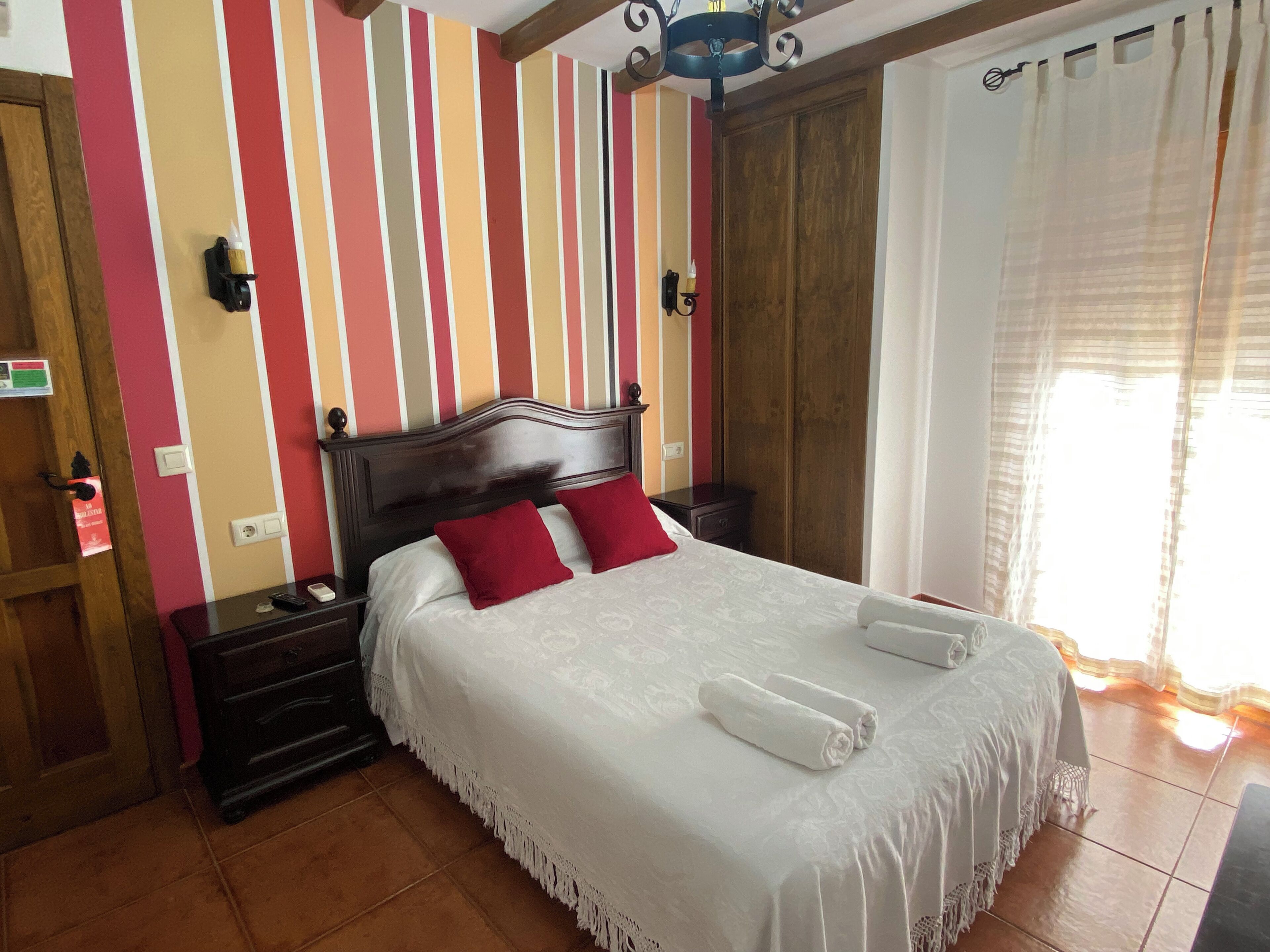 Un dormitorio con pared a rayas, cabecera de madera, mesita de noche y ventana con cortinas.