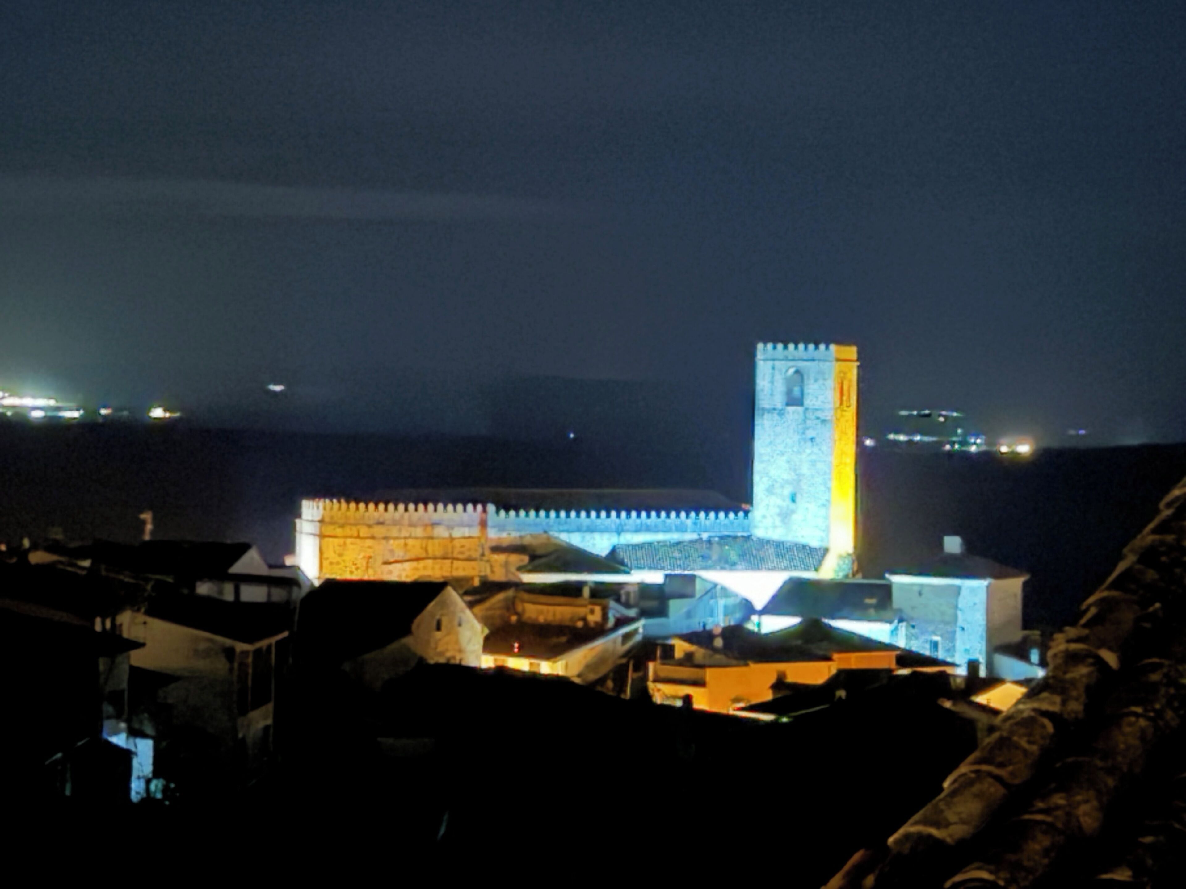 A nighttime view of a historic building with a prominent tower, surrounded by other structures.