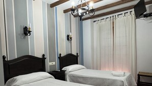 Une chambre d’hôtel avec deux lits, un lustre, une télévision et une fenêtre avec des rideaux.