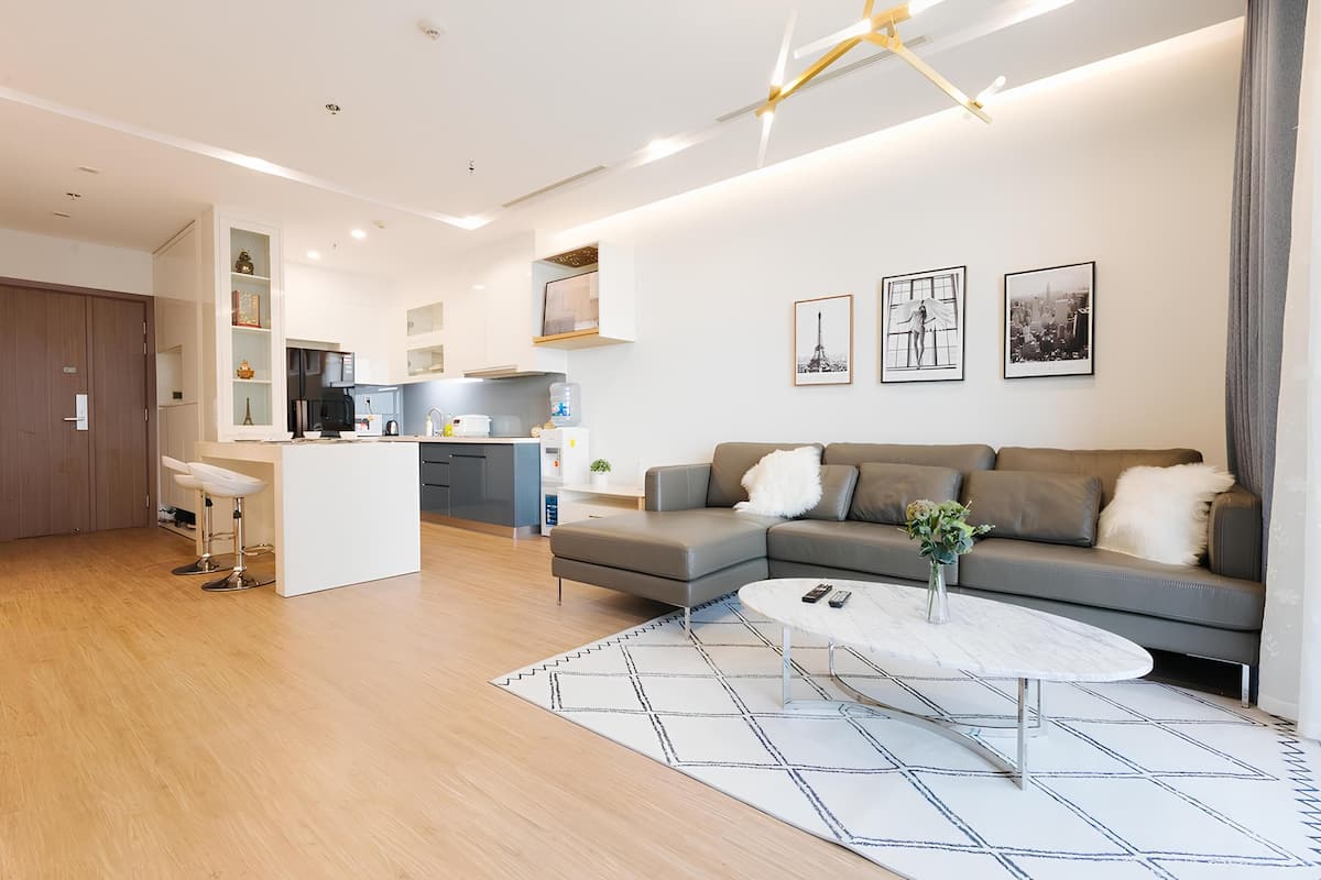 Een moderne woonkamer met een grijze bank, een witte salontafel en een keuken op de achtergrond.