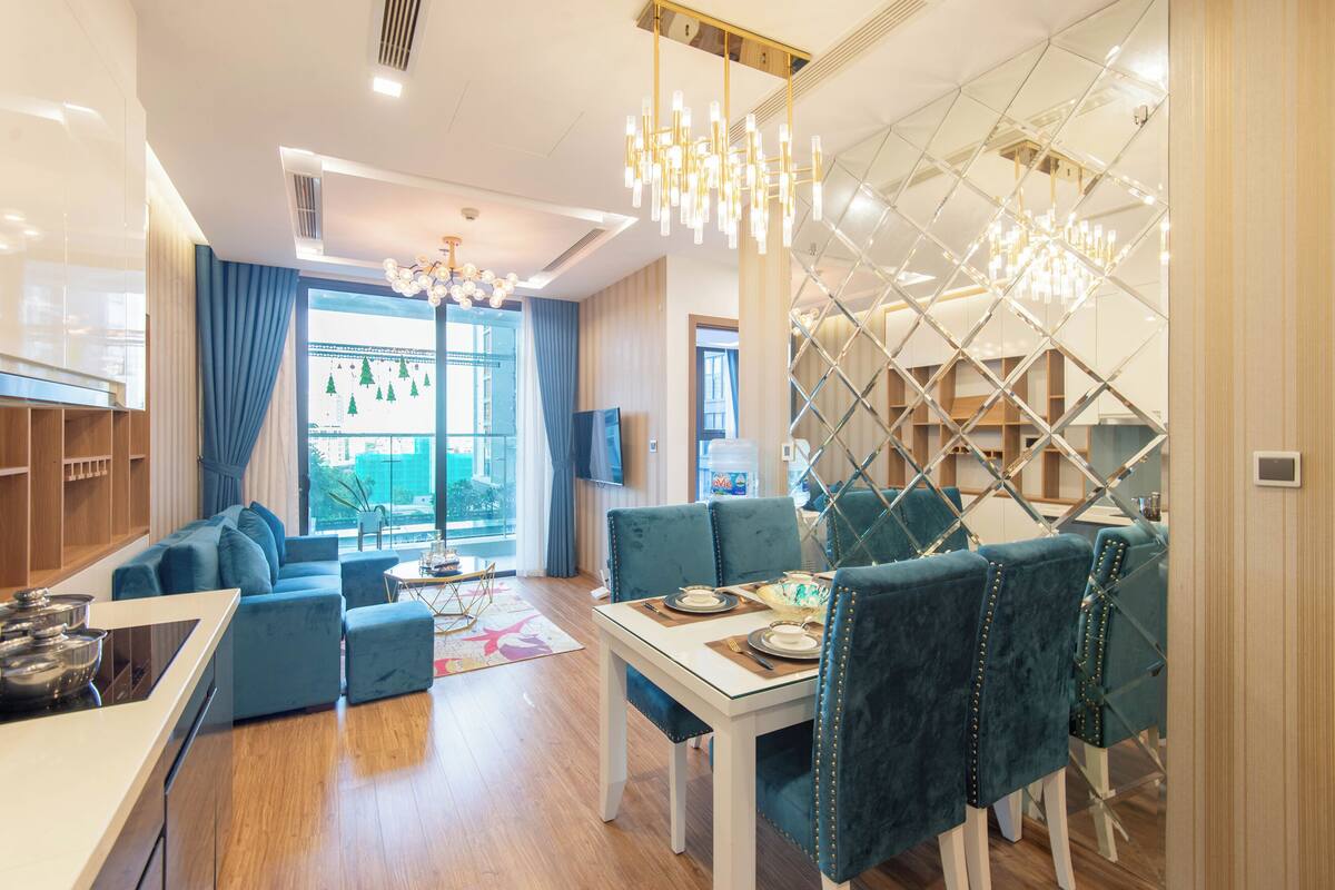 Een moderne woonkamer met een bank, eettafel en stoelen. Er is een keukenhoek met kasten en een raam.