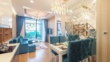 A modern living room with a sofa, dining table, and chairs. There is a kitchen area with cabinets and a window.