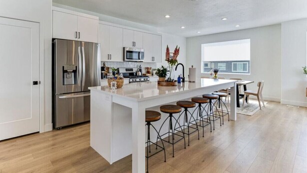 A modern kitchen with white cabinetry, stainless steel appliances, and a central island with bar stools. - Pet-Friendly | Silicon Slopes | Garage (American Fork)