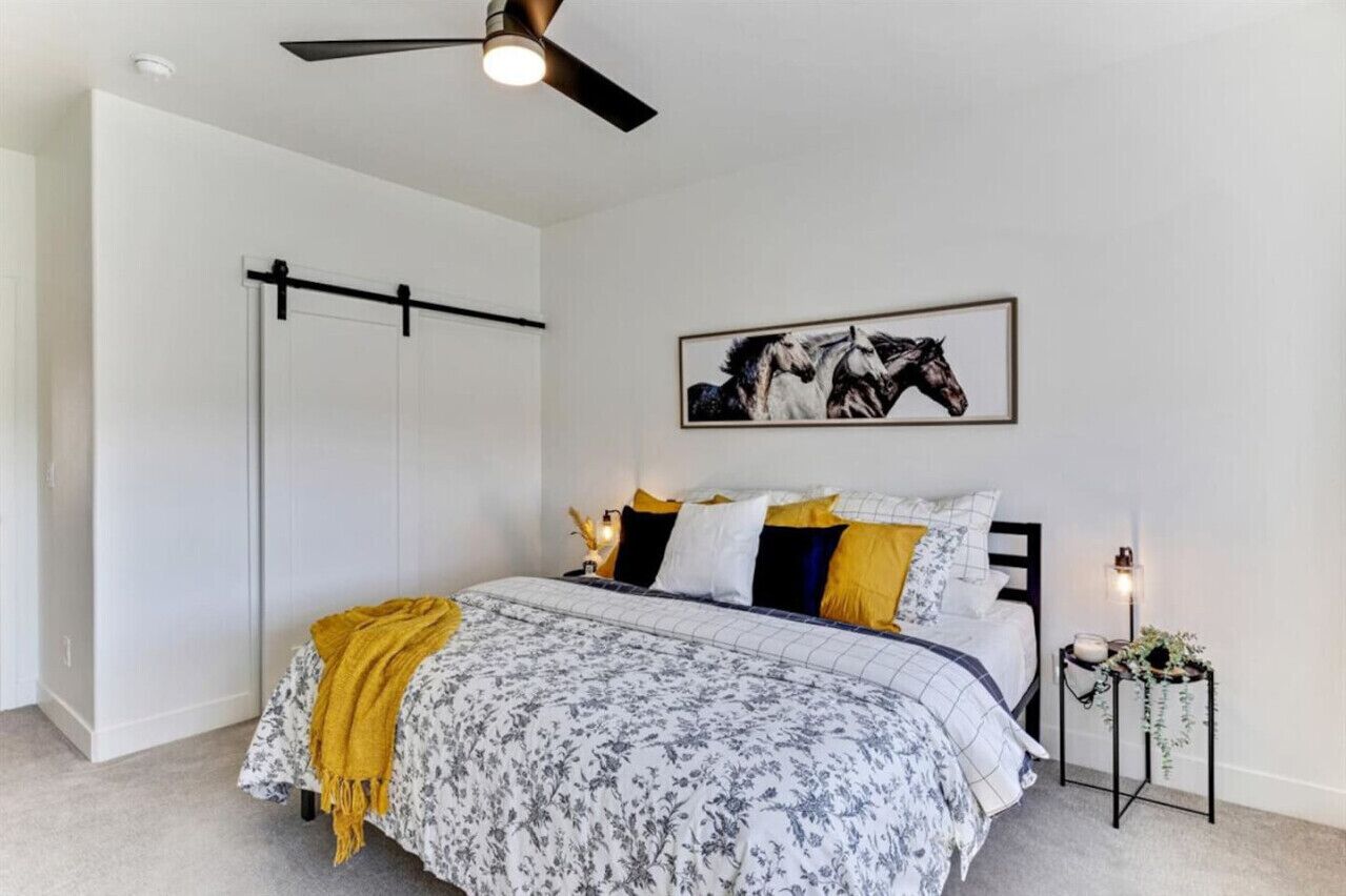 A bedroom with a bed, a ceiling fan, a framed picture, and a nightstand with a lamp.