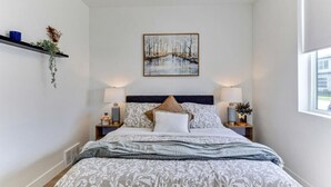 A neatly arranged bedroom with a bed, two bedside tables, a wall-mounted painting, and a window. - Pet-Friendly | Silicon Slopes | Garage (American Fork)