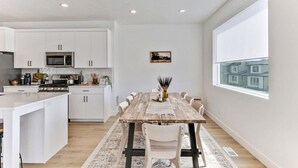 A modern kitchen with white cabinets, a central island, and a dining area with a wooden table and chairs. - Pet-Friendly | Silicon Slopes | Garage (American Fork)
