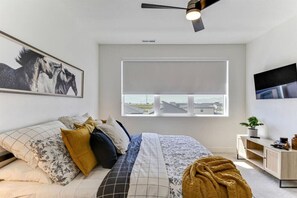 A bedroom with a bed, a ceiling fan, a window with a view, and a mounted TV.