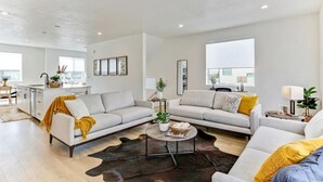 A modern living room with a sofa set, a coffee table, and a dining area with a kitchen in the background. - Pet-Friendly | Silicon Slopes | Garage (American Fork)