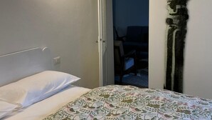 Une chambre à coucher comprenant un lit, une table de chevet, une lampe fixée au mur et une porte donnant sur une autre pièce.
