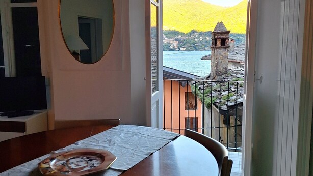 Un coin repas avec une table en bois, des chaises, un miroir rond et une vue sur un lac et des montagnes, visible à travers une porte ouverte.