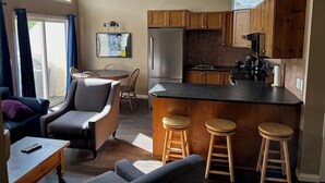 Una cocina compacta con armarios de madera, una isla central con taburetes, un refrigerador y un comedor con mesa y sillas.