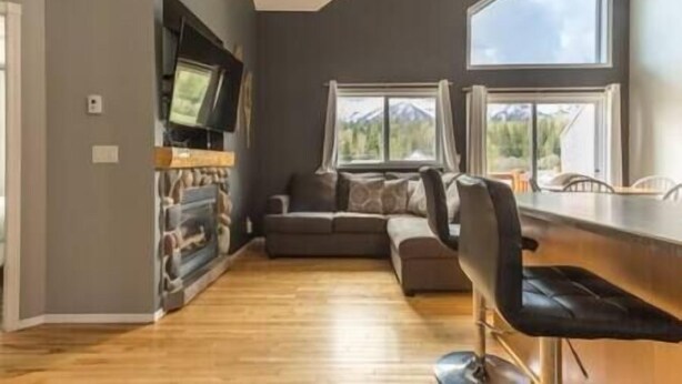 A modern living room with a fireplace, a sofa, and a dining area with a bar. - Beautiful Townhouse - Mountain Views - Sleeps 6 (Fernie)