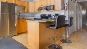 A modern kitchen with wooden cabinets, a stainless steel refrigerator, a microwave, and a coffee maker. There is a small bar area with two black bar stools. - Beautiful Townhouse - Mountain Views - Sleeps 6 (Fernie)