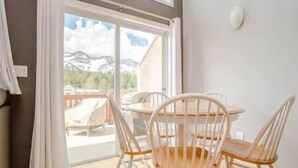 A room with a wooden floor, a round table with chairs, a large window with a view of mountains, and a white wall. - Beautiful Townhouse - Mountain Views - Sleeps 6 (Fernie)
