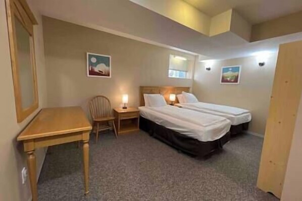 A bedroom with two beds, a desk, a chair, and two wall-mounted lamps.