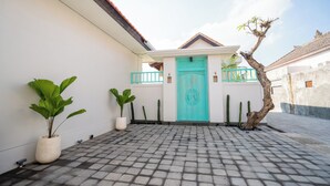 Un patio empedrado con una puerta turquesa, plantas en macetas y un árbol.