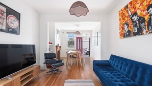 Ein modernes Wohnzimmer mit einem Flachbildfernseher, einem blauen Sofa, einem Esstisch mit Stühlen und einem Holzschrank.
