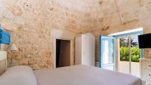 A bedroom with a stone wall, a bed, a wardrobe, and a TV. - 3985 Tenuta di Uma by Barbarhouse (Carovigno)