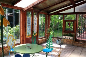 A covered patio with a round table and chairs, large windows with decorative glass, and a view of greenery.