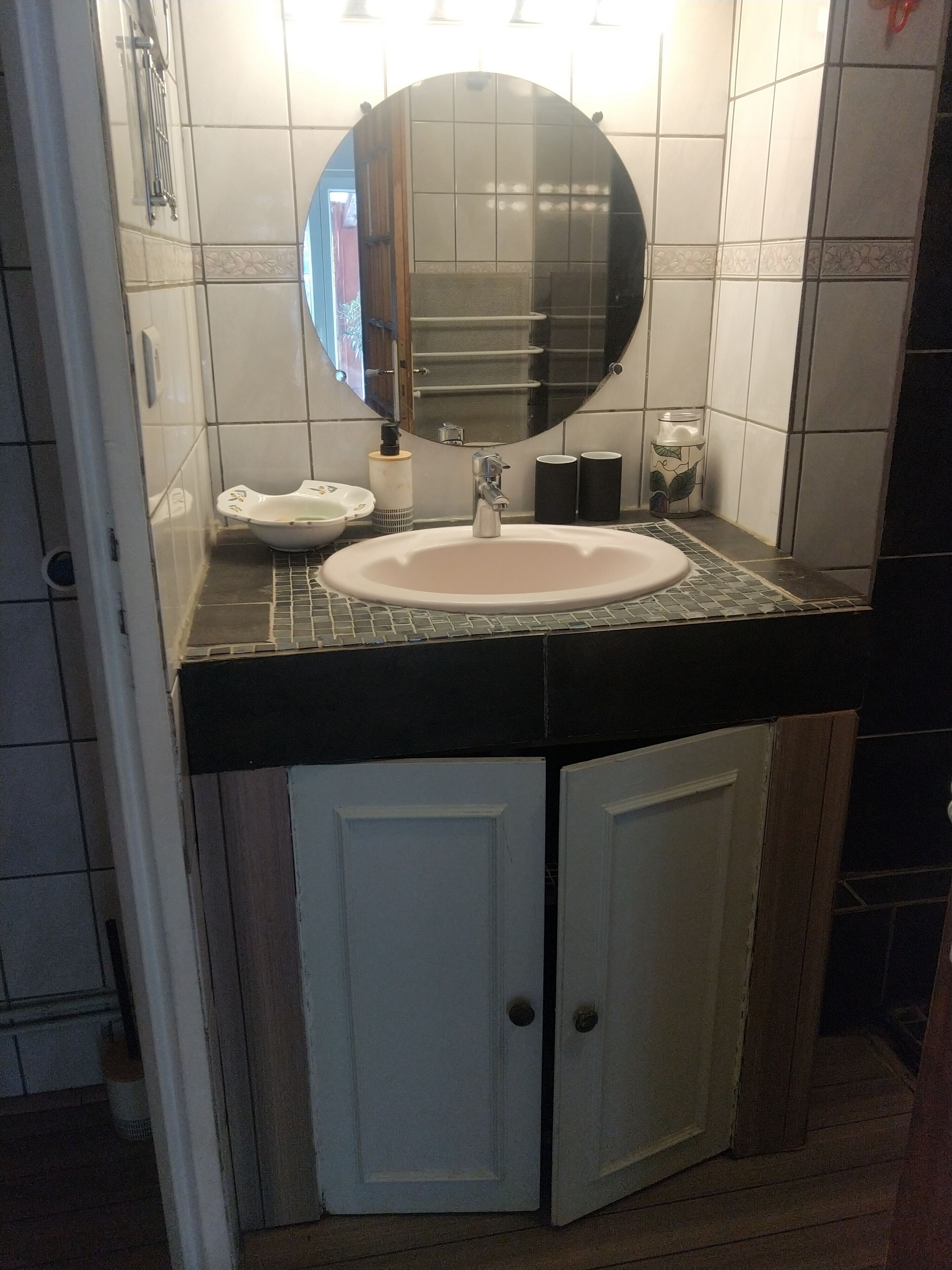 Une salle de bain avec un lavabo blanc, un miroir et deux armoires blanches.