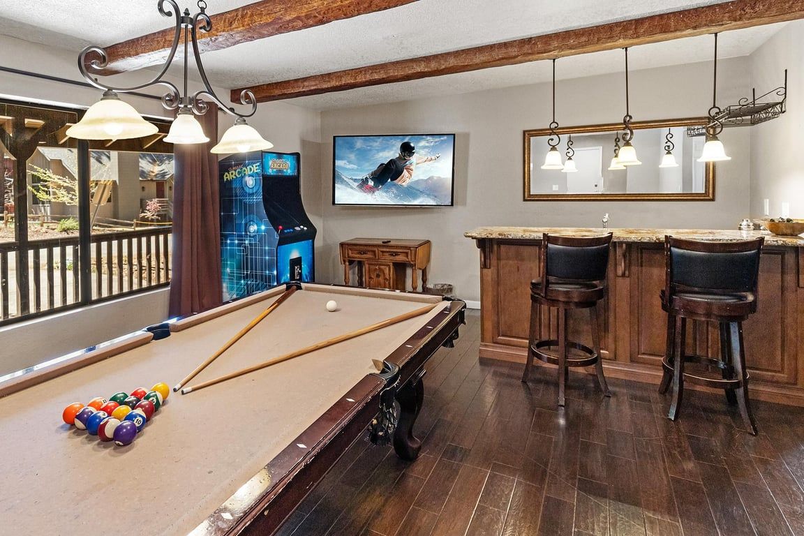 A pool table with balls, a bar area with stools, and a television displaying a snowboarder.