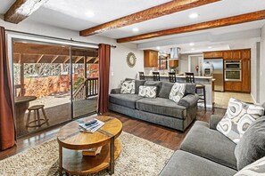 A modern living room with a sofa, coffee table, and a view of the kitchen and outdoor area.