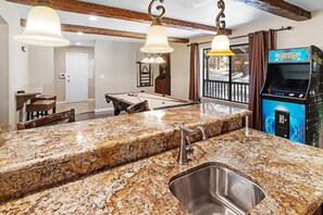 A kitchen with granite countertops, a stainless steel sink, and a pool table.
