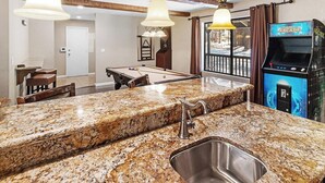 Una cocina con encimera de granito, pileta de acero inoxidable y una mesa de billar.