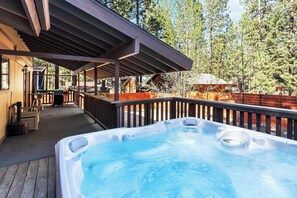 A hot tub on a wooden deck with a covered patio area and a view of trees.