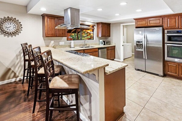 A modern kitchen with a central island, wooden cabinets, stainless steel appliances, and a decorative clock on the wall.