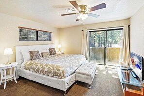 A bedroom with a large bed, a ceiling fan, a window with curtains, and a television on a glass table.