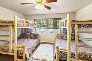 A room with three bunk beds, a ceiling fan, and a window with a view of trees.