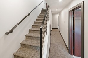 A carpeted staircase with a handrail and a wooden door at the bottom. - Clip In and Ride Straight Onto Chair 9 at Bear Mountain! Private HOT TUB! Air Conditioning! Pickle Ball Court! EV Charger! (Big Bear Lake)