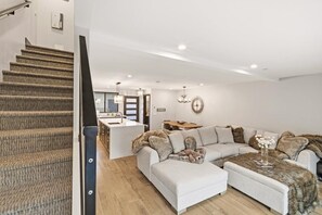 A modern interior with a staircase, a living area with a sofa and ottoman, a kitchen area, and a dining table.