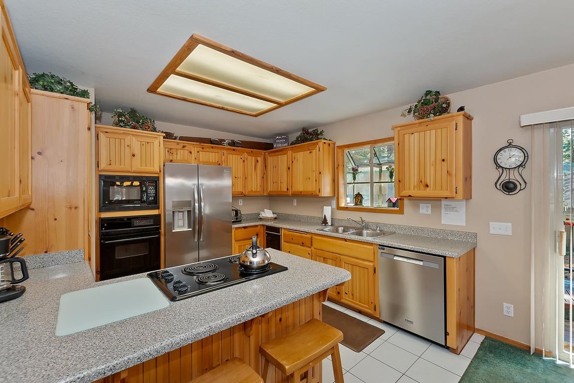 A kitchen with wooden cabinets, stainless steel appliances, a granite countertop, and a window with a view.