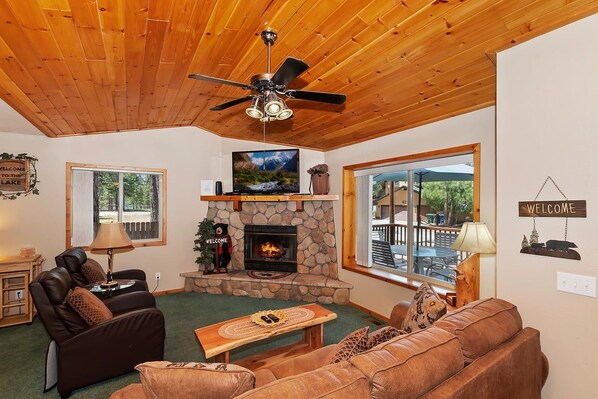 A cozy living room with a fireplace, leather sofas, a wooden ceiling, and a television.