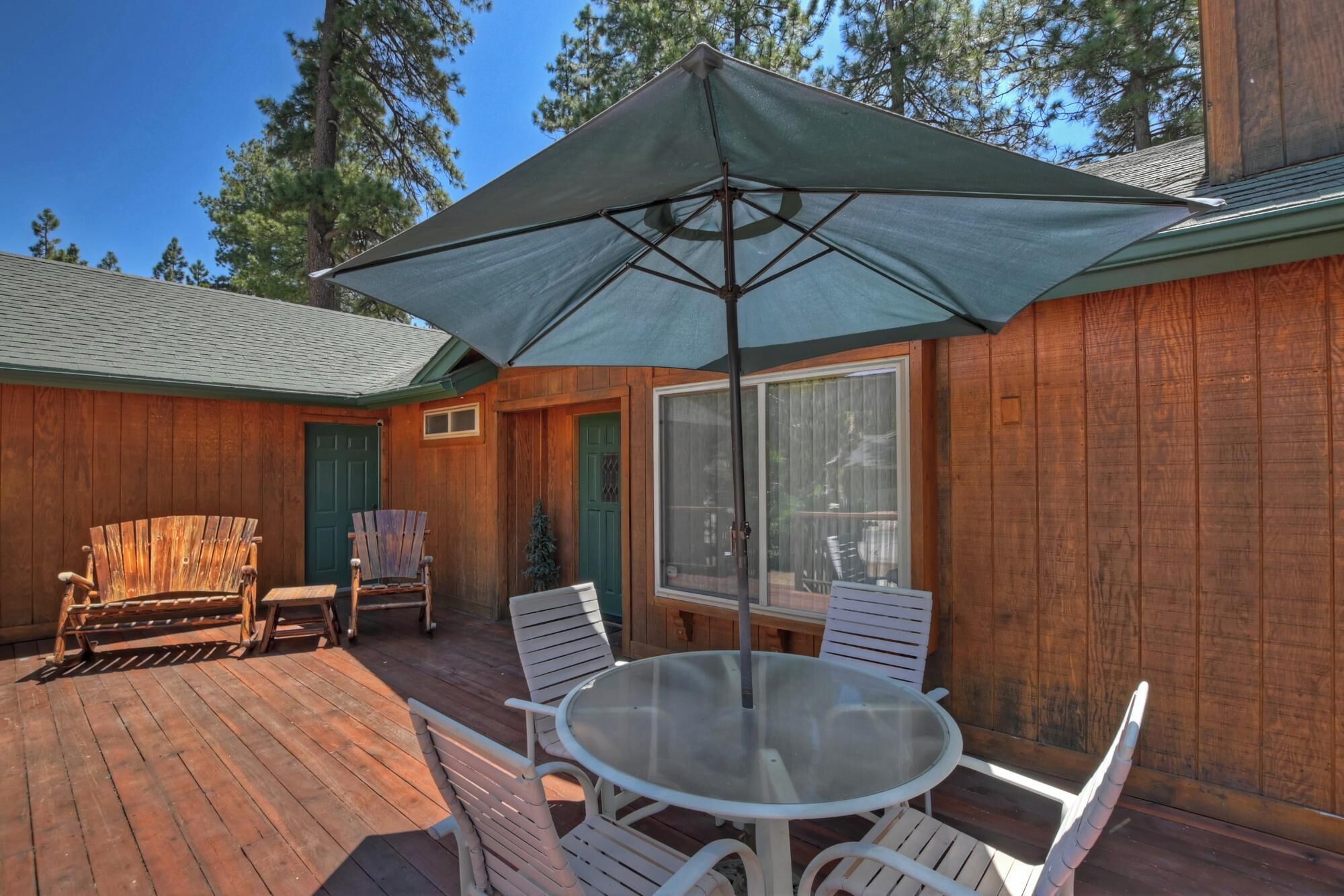 A wooden deck with a glass table and chairs, a large umbrella, and a wooden chair.
