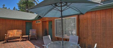 A wooden deck with a glass table and chairs, a large umbrella, and a wooden chair.