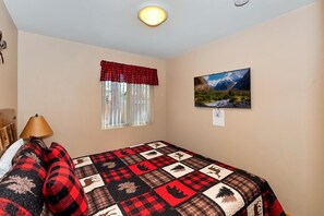 Um quarto com uma cama, uma janela com cortinas, um quadro na parede e um abajur.