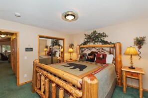 A room with a bed featuring a wooden headboard, a mirror, a nightstand with a lamp, and a sign on the wall.