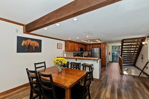 A dining area with a wooden table and chairs, a kitchen with wooden cabinets, and a staircase.