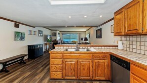 A spacious kitchen with wooden cabinets, a central island, and a view to the outside. - Lakefront Haven:Lakefront Condo! Located in the Village! Community Spa & Pool! Private Dock! (Big Bear Lake)