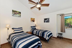 A bedroom with two beds, a ceiling fan, and a window with a view of greenery.