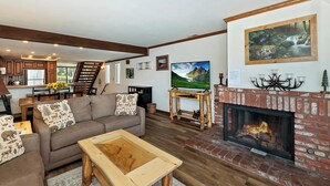 A living room with a fireplace, a sofa, a coffee table, and a TV. - Lakefront Haven:Lakefront Condo! Located in the Village! Community Spa & Pool! Private Dock! (Big Bear Lake)