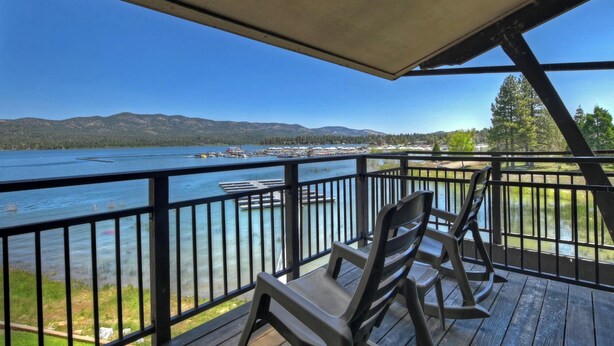 A deck with a view of a lake, docked boats, and mountains in the distance. - Lakefront Haven:Lakefront Condo! Located in the Village! Community Spa & Pool! Private Dock! (Big Bear Lake)