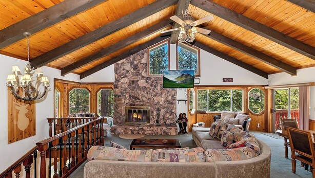 A spacious living area with a stone fireplace, wooden beams, and large windows offering views of the outdoors.
