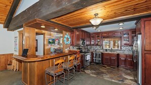 A kitchen with wooden cabinets, a bar area with stools, and a large stove.