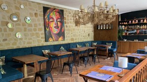 Ein Restaurant mit Holztischen, blau gepolsterten Sitzmöglichkeiten, Steinwänden und einem farbenfrohen Gemälde.