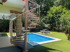 A pool area with a staircase leading to a covered deck, surrounded by lush greenery. - 175 MBPS internet, private pool, golf, beaches and Ojochal (San Buena)